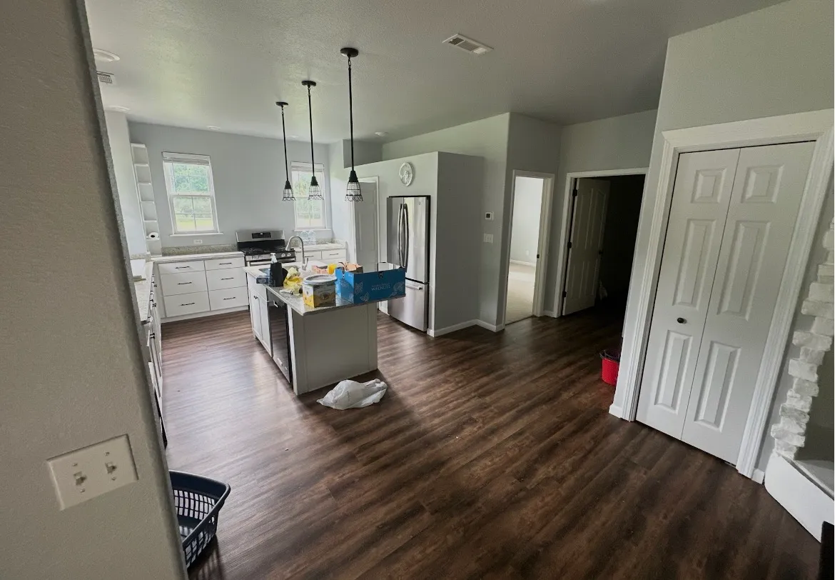 Open-concept kitchen and living area before its refresh, with dark walnut-look plank flooring, cool gray walls, and belongings still being moved into the space