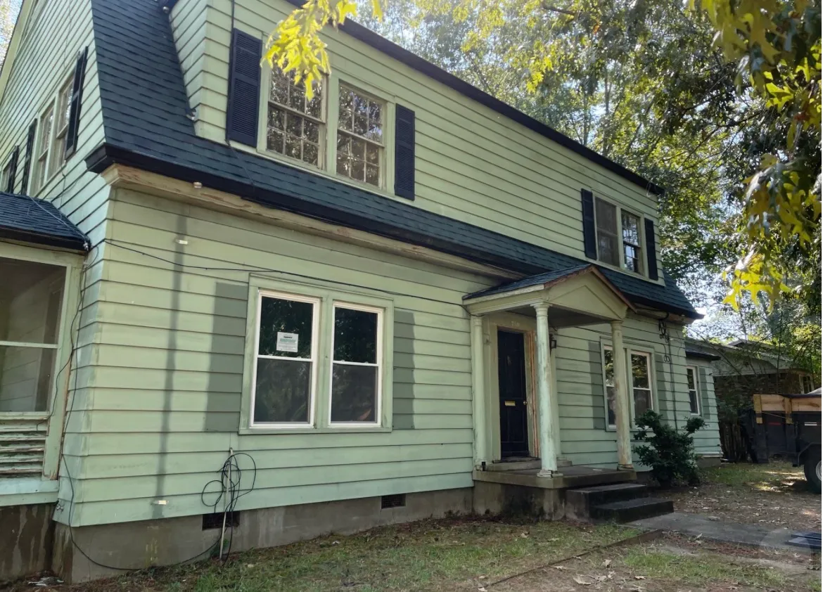 Two-story home after exterior painting, with fresh sage-green siding, black shutters, a black roof, and a newly finished columned front porch