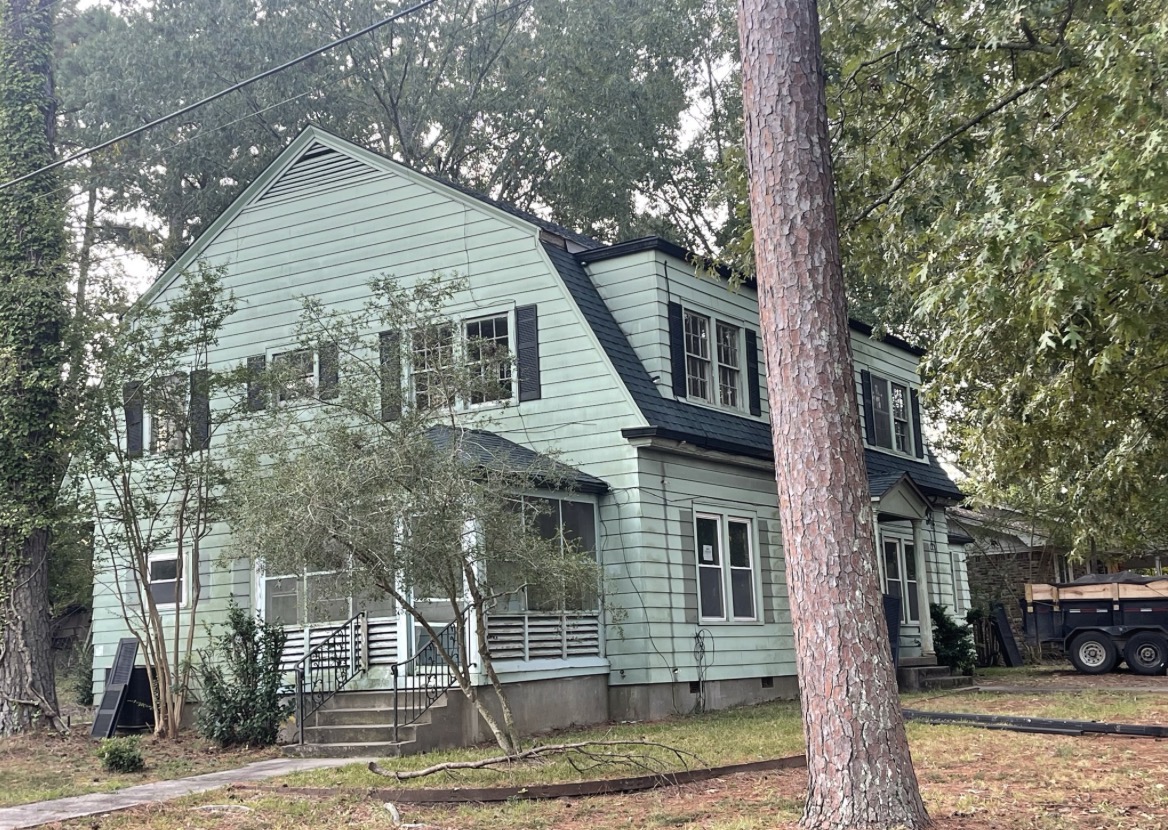 Side view of the same home after exterior painting, with clean sage-green clapboard siding and a black gambrel roof