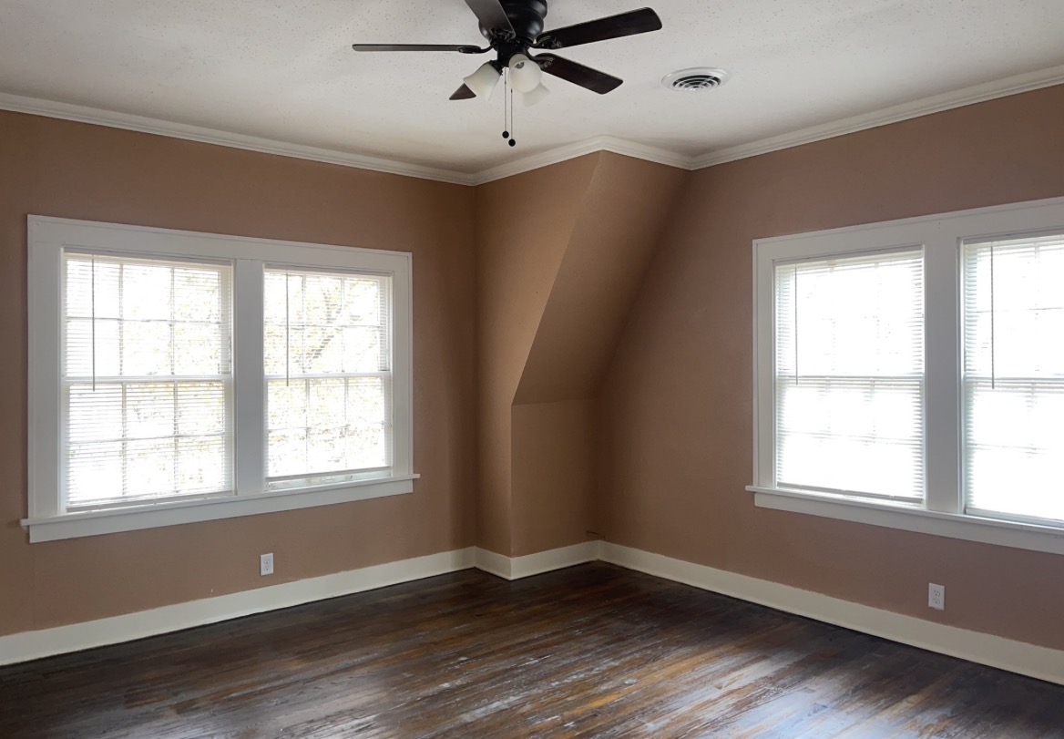 Interior painting in progress in a living room, with walls prepped, windows masked off, and floors covered with drop cloths
