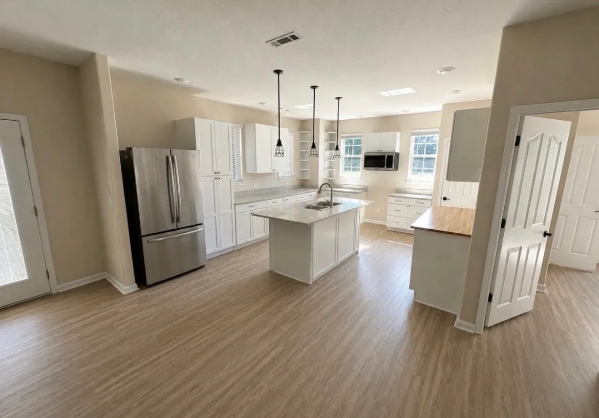 Remodeled open-concept kitchen with white shaker cabinets, a granite island with sink, stainless refrigerator, and light wood-look plank flooring
