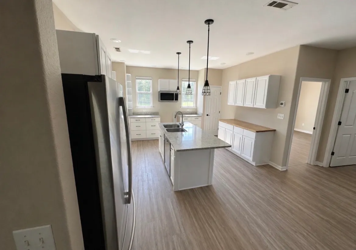 Bright remodeled kitchen with white cabinetry, a center island, butcher-block counter run, and pendant lighting