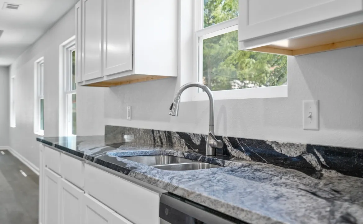 Remodeled kitchen with white cabinets, a dark veined granite countertop, stainless pull-down faucet, and a window above the sink
