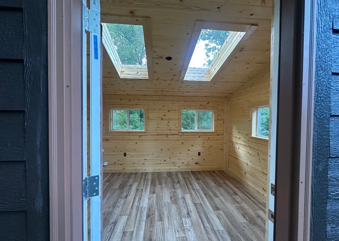 The same shed interior finished with warm pine tongue-and-groove walls and ceiling, twin skylights, and light wood-look plank flooring
