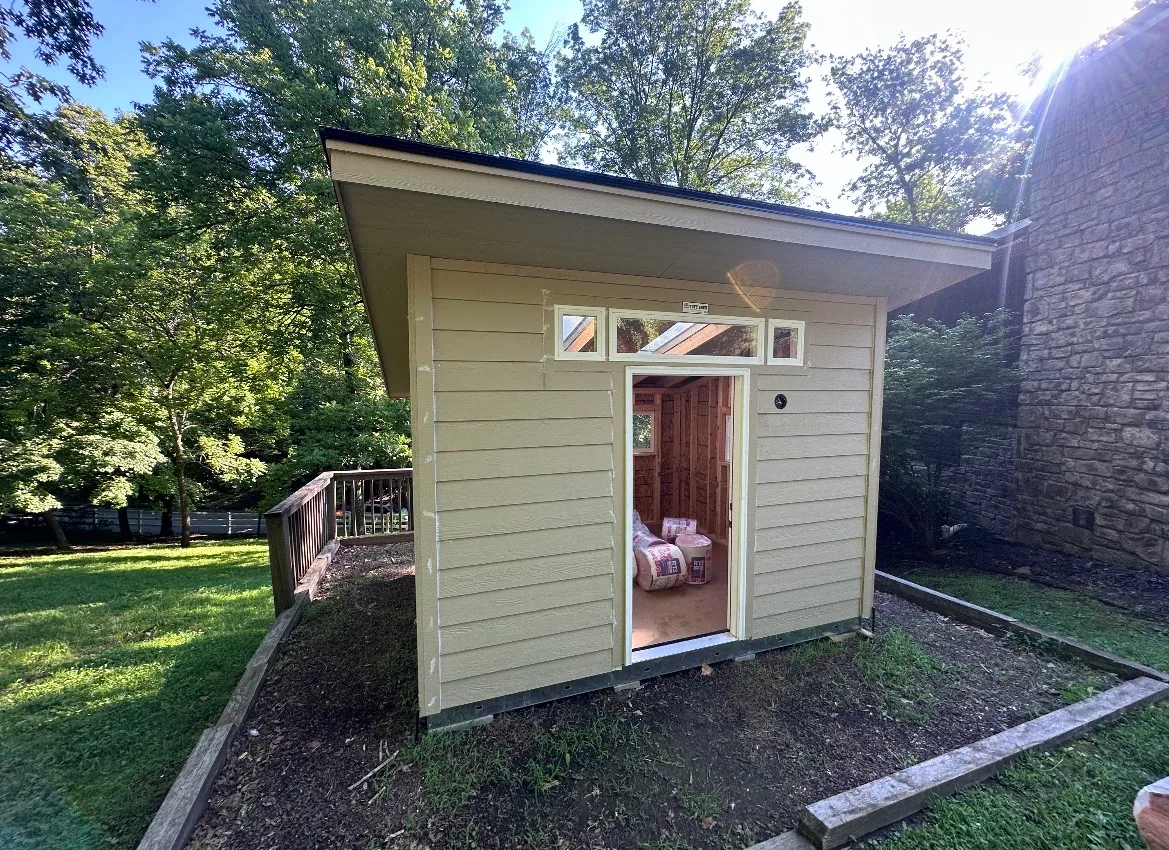 Shed during the build, with unpainted tan LP siding, an open doorway, and insulation still stacked inside