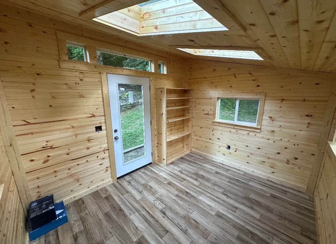 Finished shed interior with pine tongue-and-groove walls, skylights, built-in shelving, and vinyl plank flooring