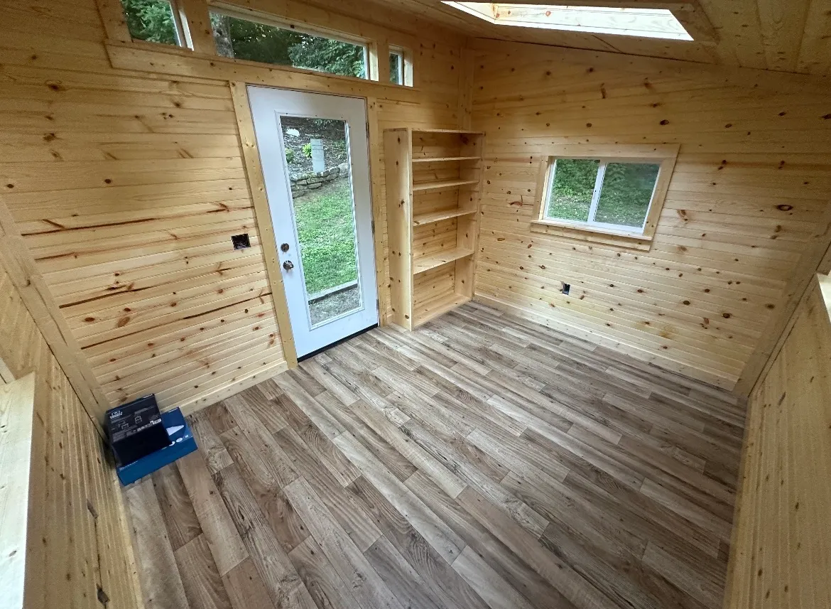 Interior of a finished backyard studio with wood-lined walls, a glass door, and durable plank flooring