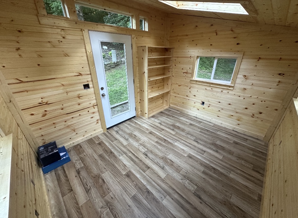 Interior of a finished backyard studio with wood-lined walls, a glass door, and durable plank flooring