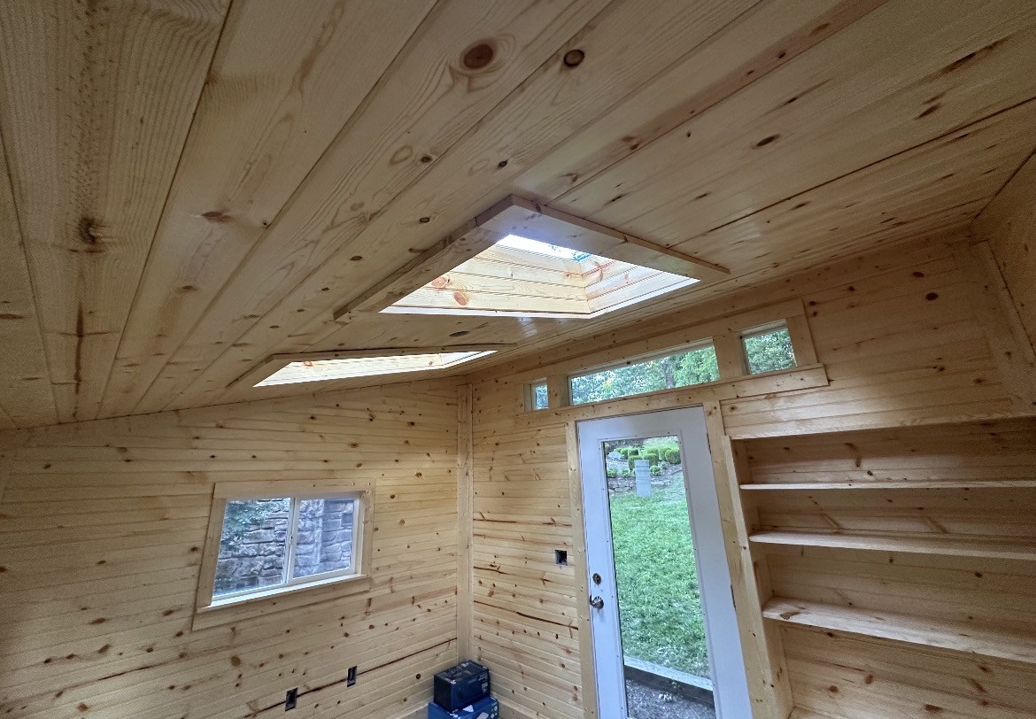 Vaulted shed ceiling with skylights and pine paneling above a bright finished interior